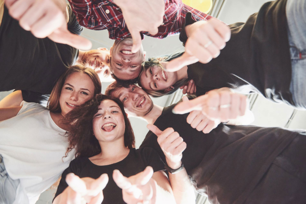 Un groupe de 6 jeunes personnes souriantes positionnées en cercle au-dessus de l'appareil photo qui les prend en plongée.